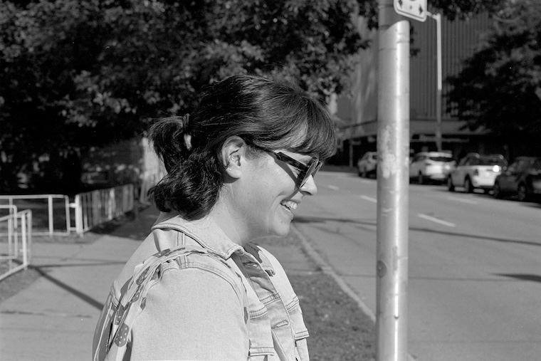 Photo of Kathleen, a woman with brown hair, stifling a laugh on a street corner as I made a number of photos of her. Click for full size.